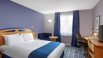 Una habitación de hotel con una cama grande, un escritorio con silla, un televisor y una ventana con cortinas.