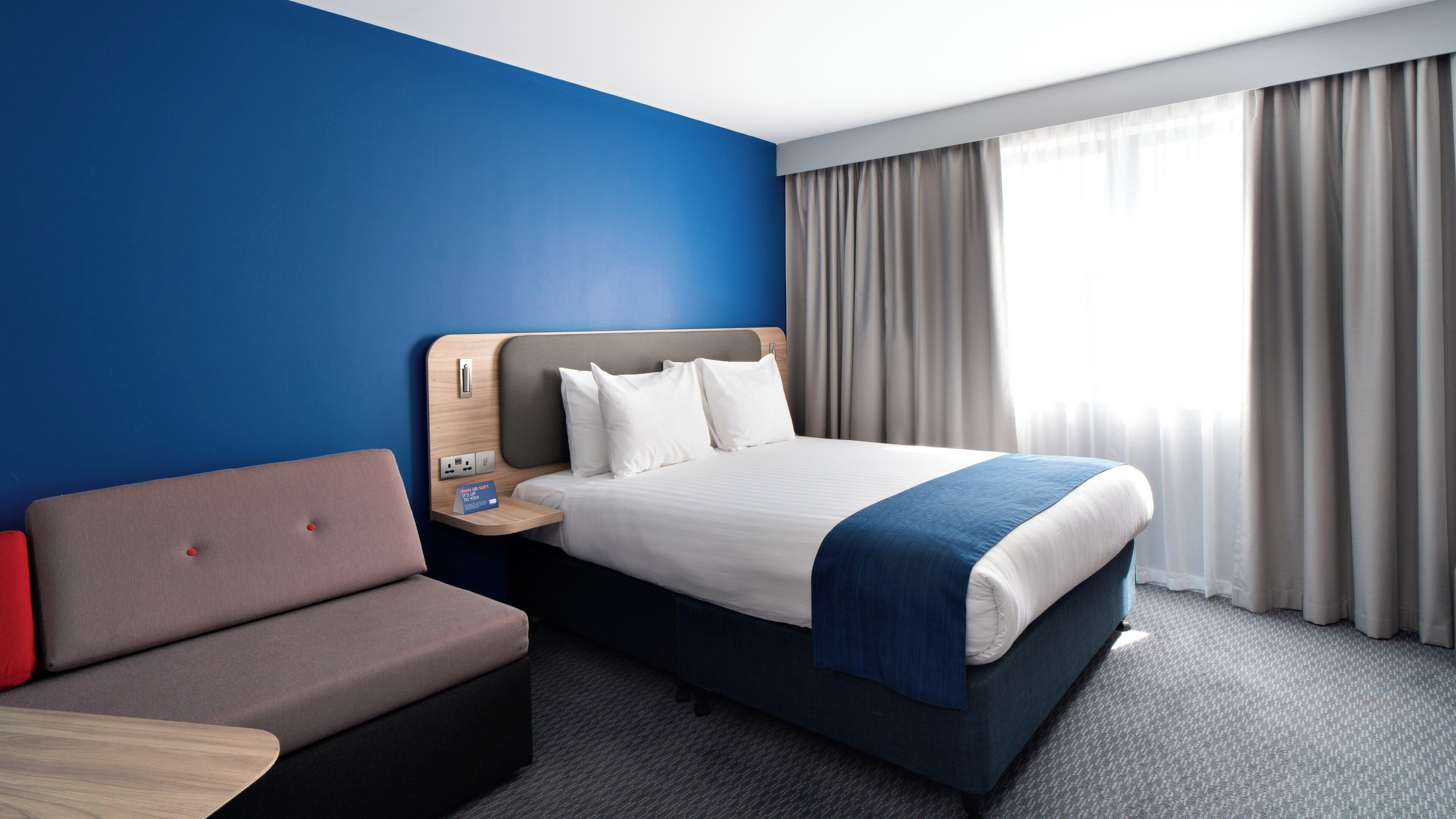 Une chambre d’hôtel avec un lit, un canapé, une table de chevet et une fenêtre avec des rideaux.