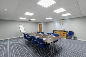 A conference room with a long table, blue chairs, a whiteboard, and a clock on the wall.