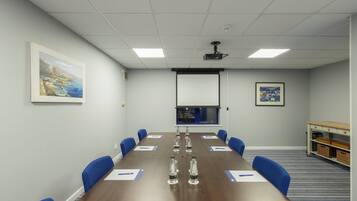 A conference room with a long table, blue chairs, water bottles, and a projector screen.