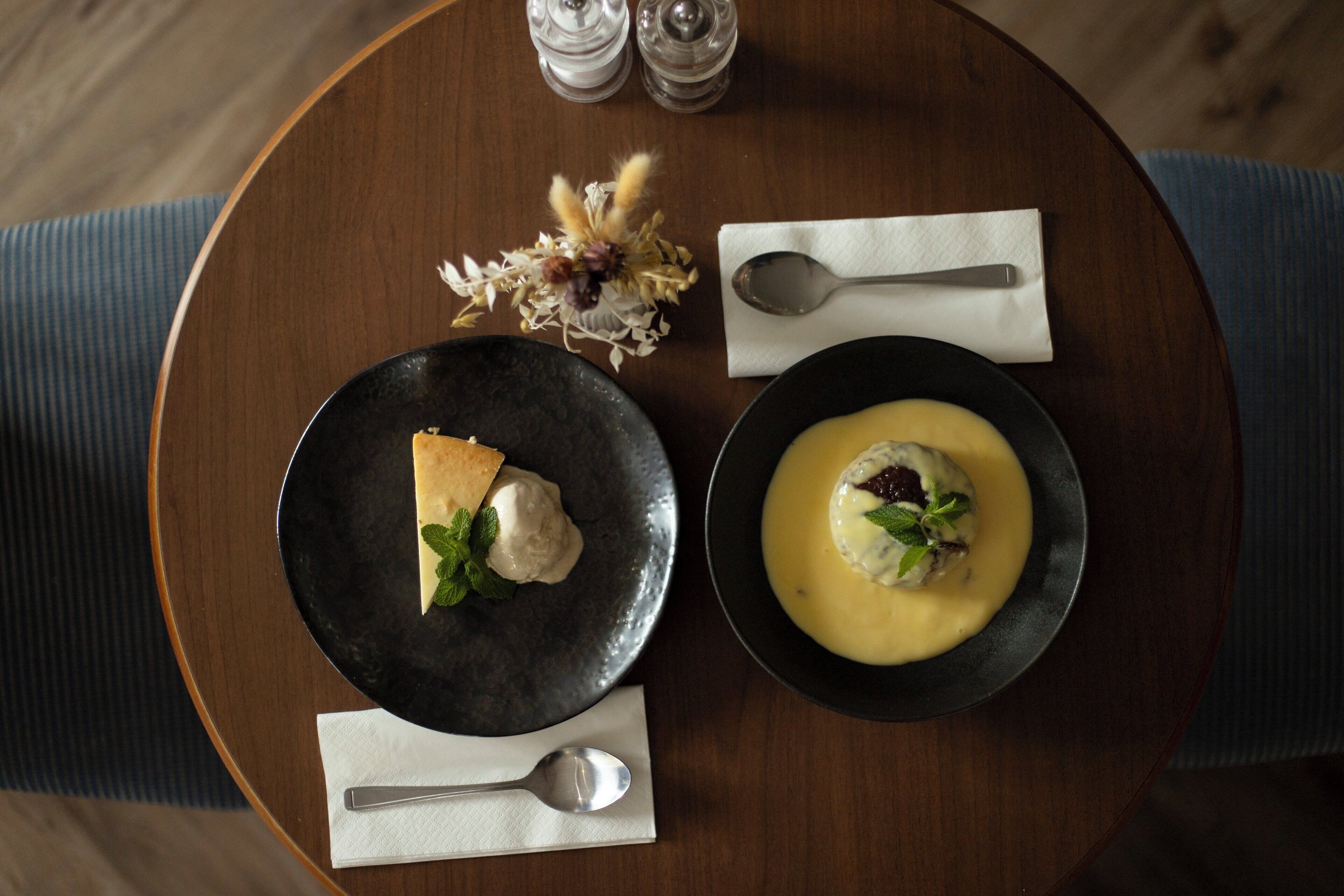 A round wooden table with two plates of food, a spoon, and a napkin.