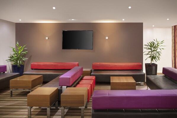 A modern lounge area with multiple seating options, including sofas and tables, and a flat-screen TV mounted on the wall.