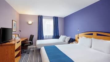 A hotel room with a bed, a desk with a TV, a chair, and a window with curtains.