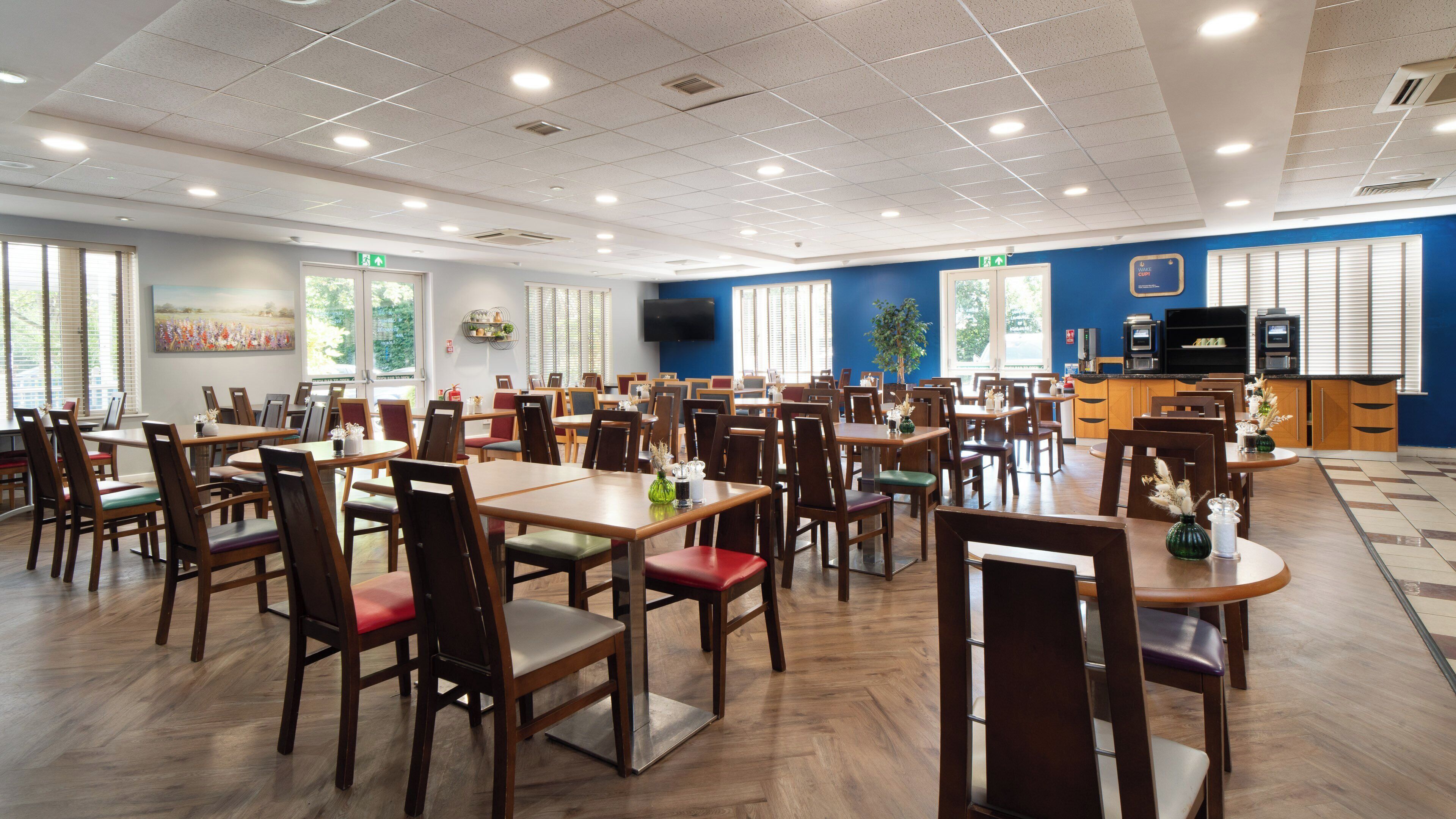 A spacious dining area with multiple tables and chairs, a television, and a kitchen area.