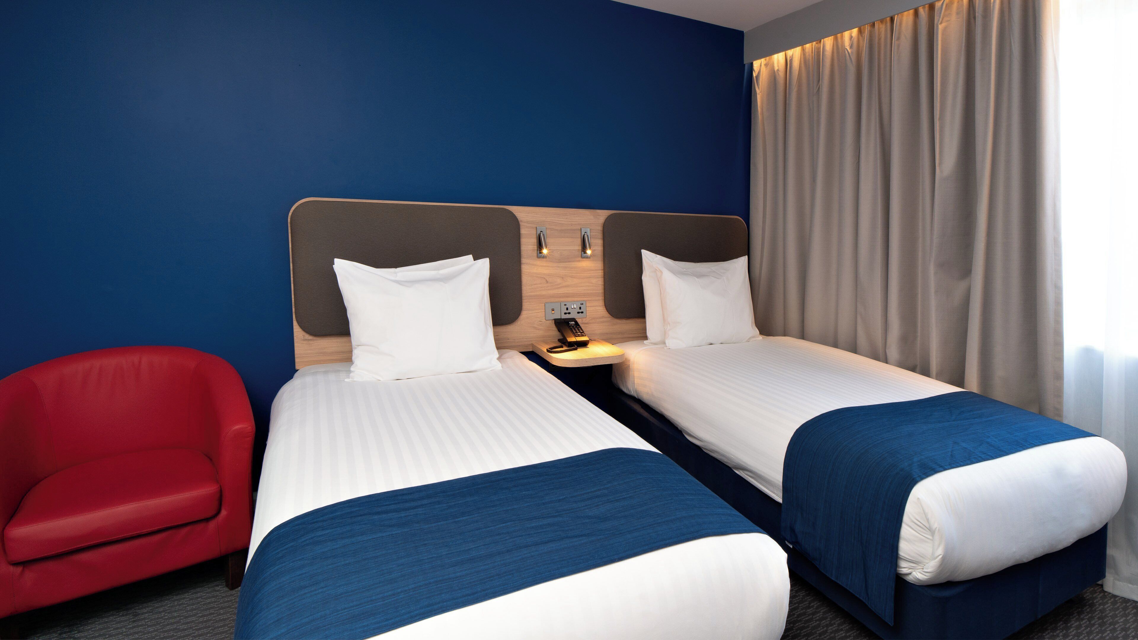 A hotel room with two beds, a red chair, and a wooden headboard.