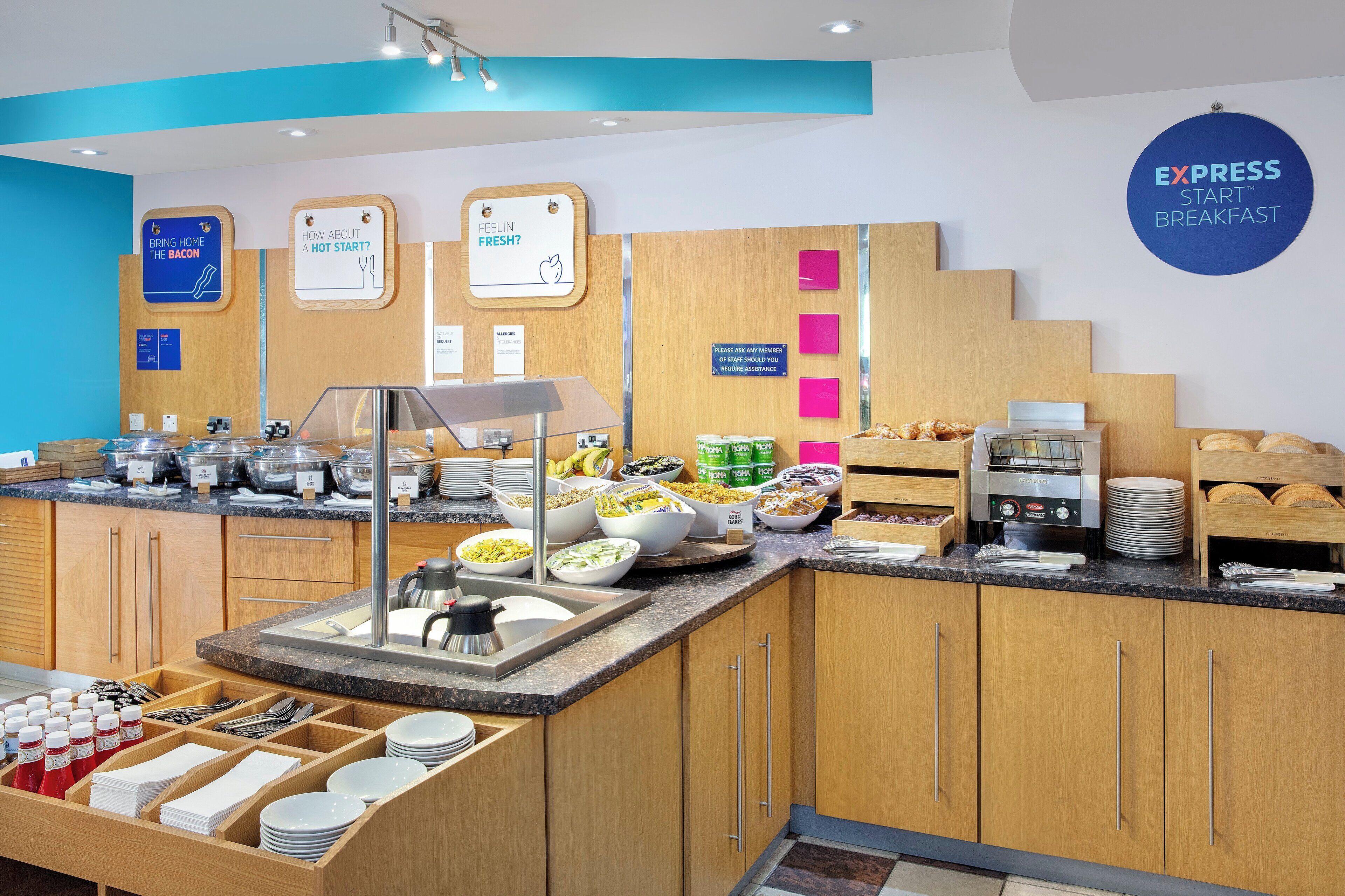 A breakfast buffet area with various food options, a coffee machine, and a sign indicating breakfast availability.