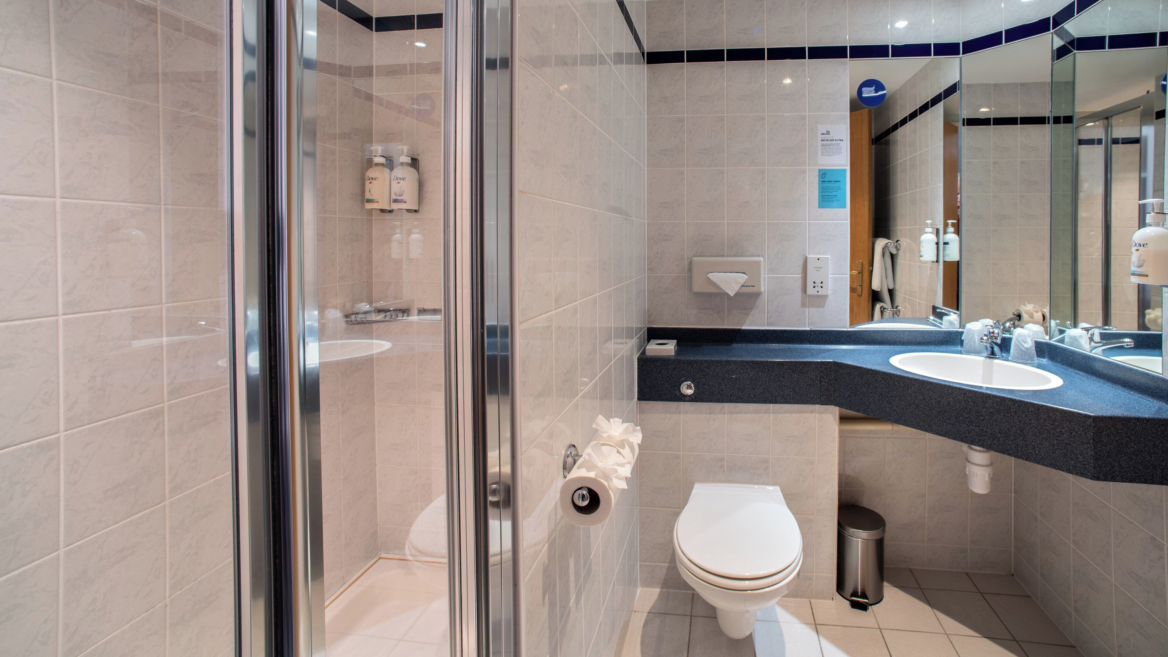 Ein modernes Badezimmer mit einer Duschkabine aus Glas, zwei Waschbecken, einer Toilette und einem großen Spiegel.