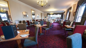 A hotel dining area with multiple tables and chairs, a red carpet, and chandeliers. - The Minster Hotel York (York)