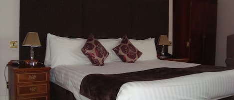 Una cama bien hecha con un cabecero oscuro, dos lámparas de noche y una mesita de noche de madera con cajones.