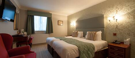 A hotel room with a large bed, a desk with a chair, a television, and a window with curtains.