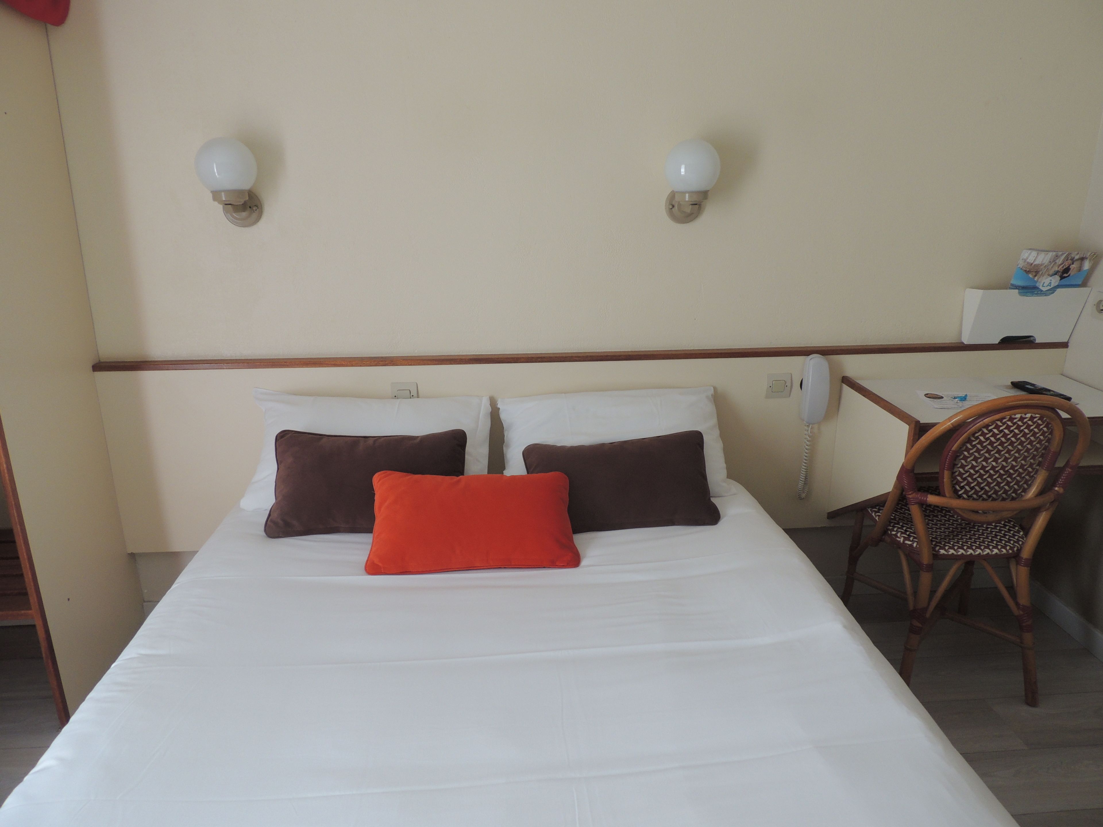 Una habitación de hotel con una cama, dos almohadas, una silla, un escritorio y un teléfono.