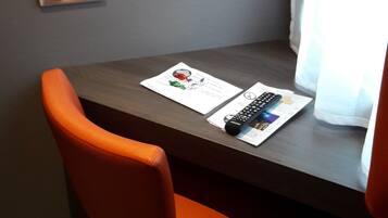 A small table with a chair, a power outlet, and a window with curtains.