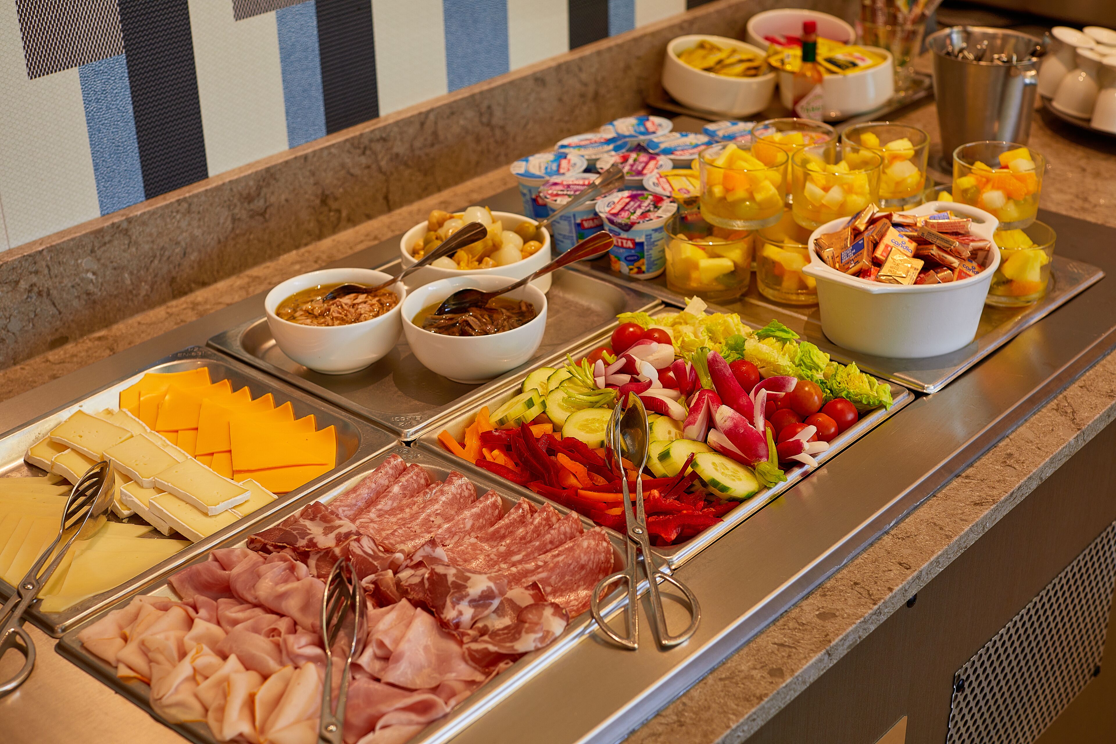 A buffet with various food options including meats, cheeses, fruits, and vegetables.
