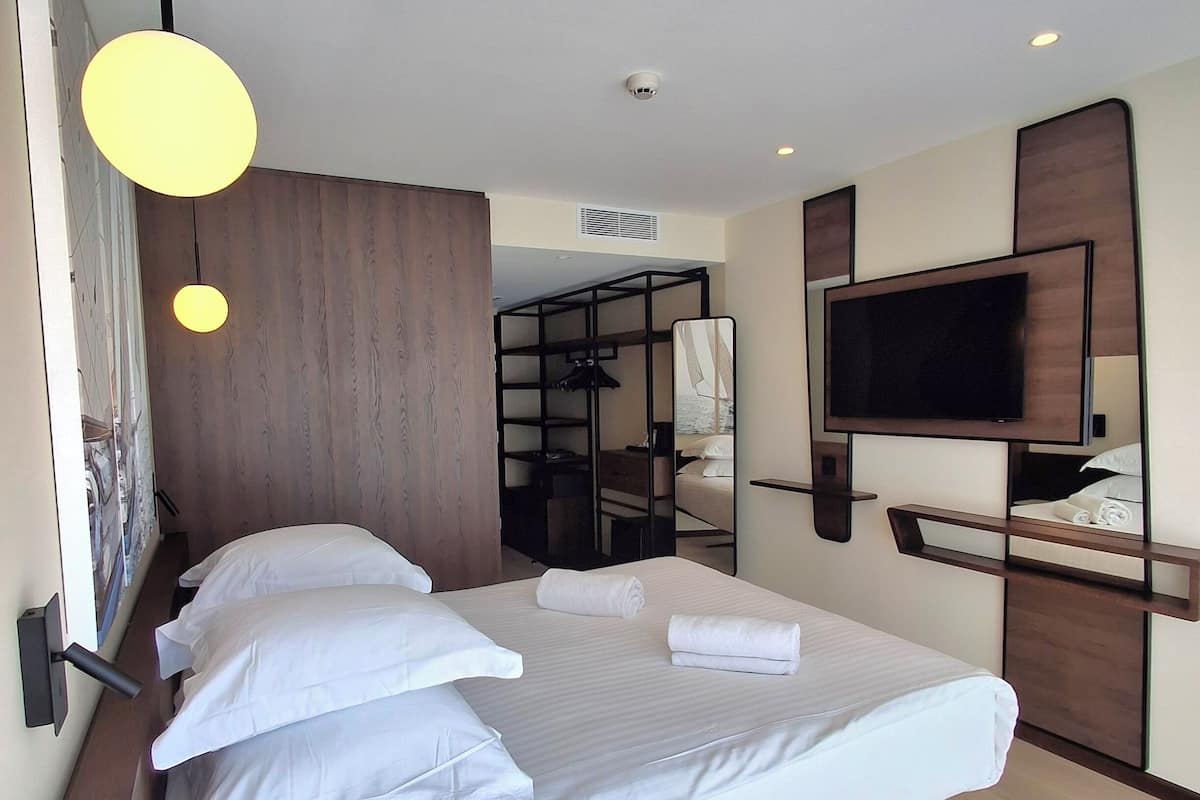 A modern hotel room with a large bed, a flat-screen TV mounted on the wall, and a wooden wardrobe.