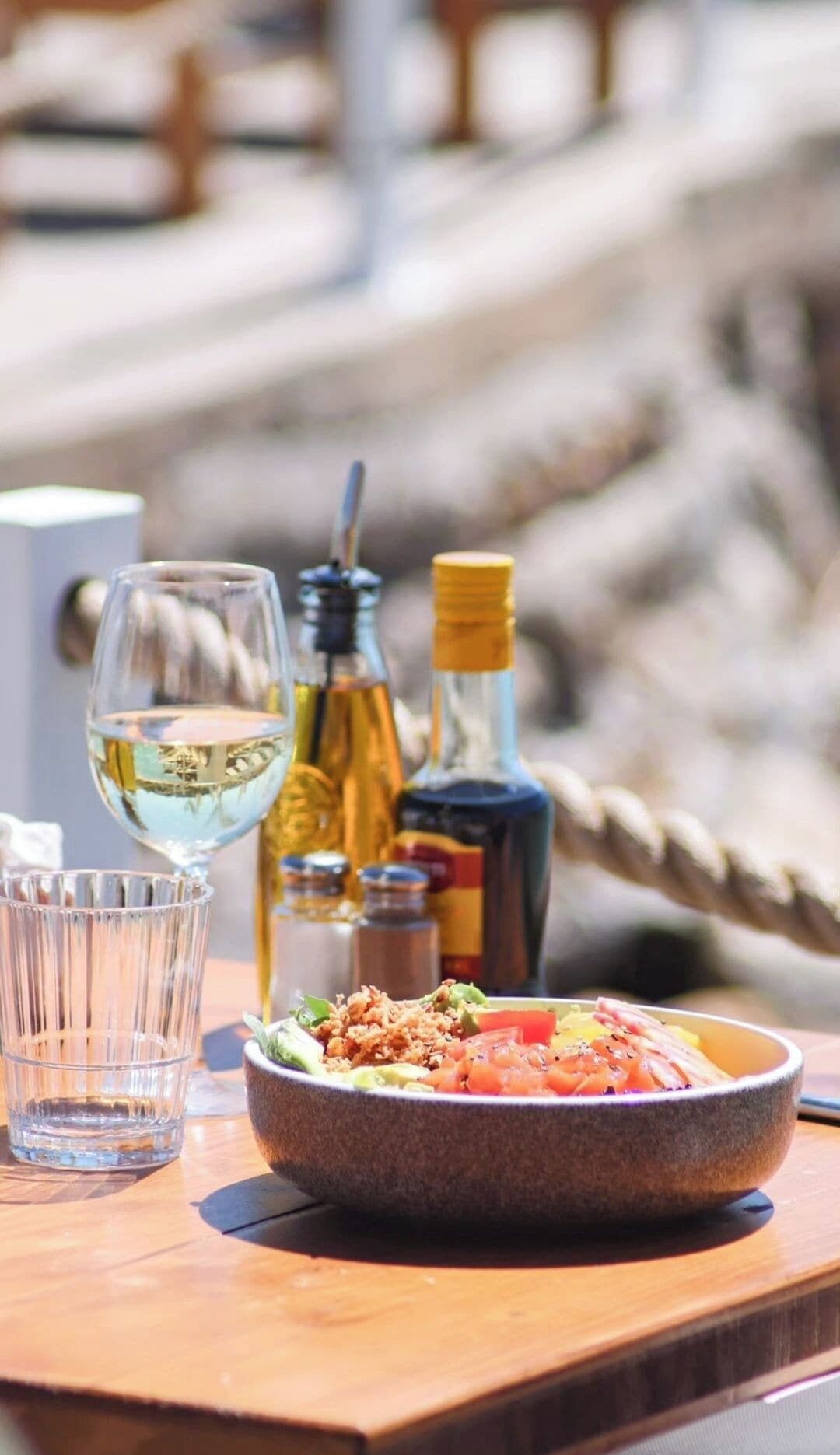 A table with a meal, a glass of white wine, and two bottles of olive oil.