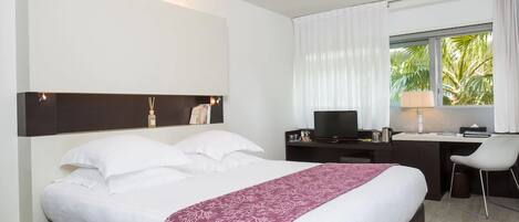 Quarto de hotel com uma cama, uma escrivaninha com computador, uma cadeira e uma janela com cortinas.