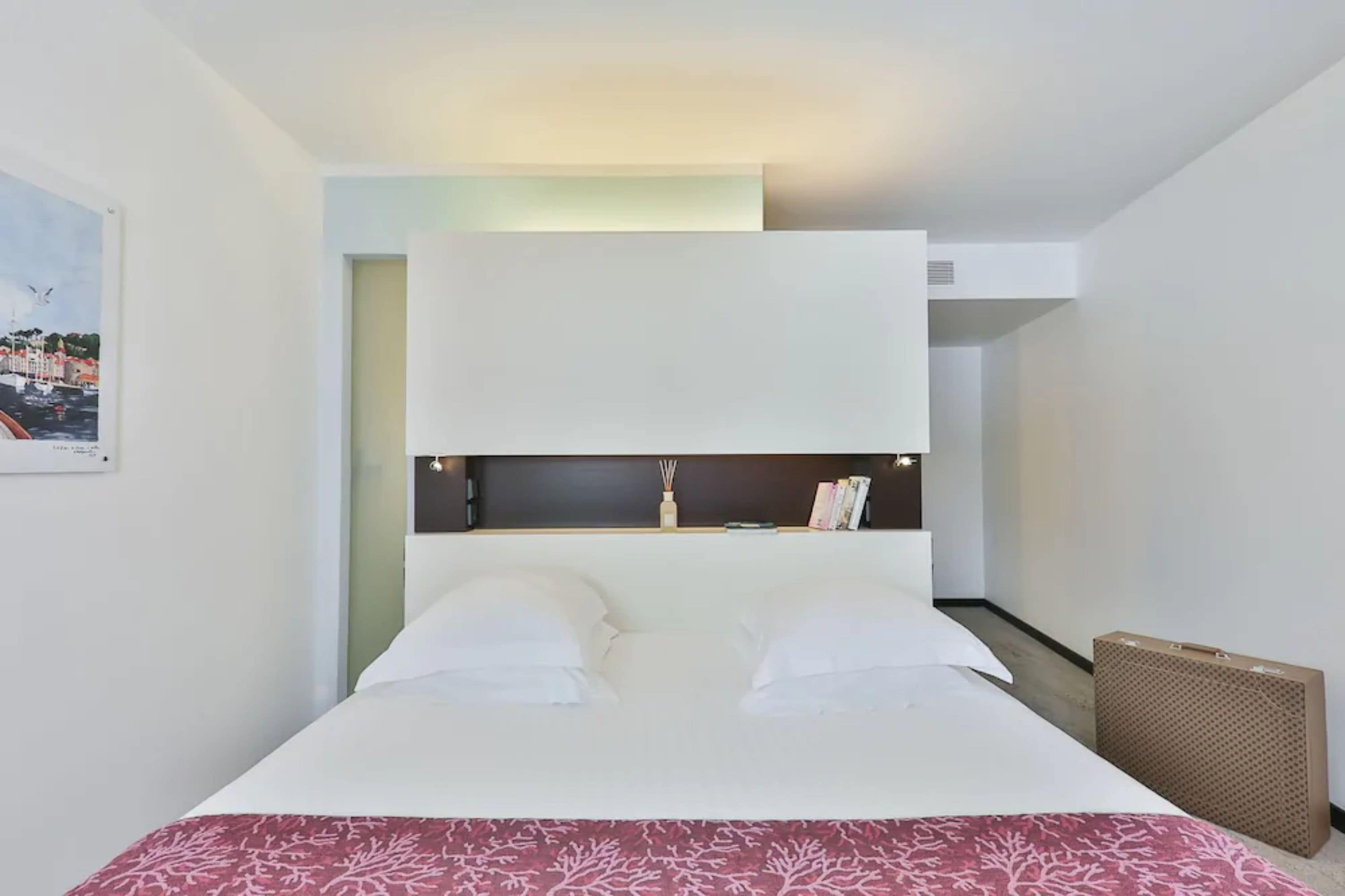 A modern hotel room with a large bed, a headboard with a shelf, and a view of the city.