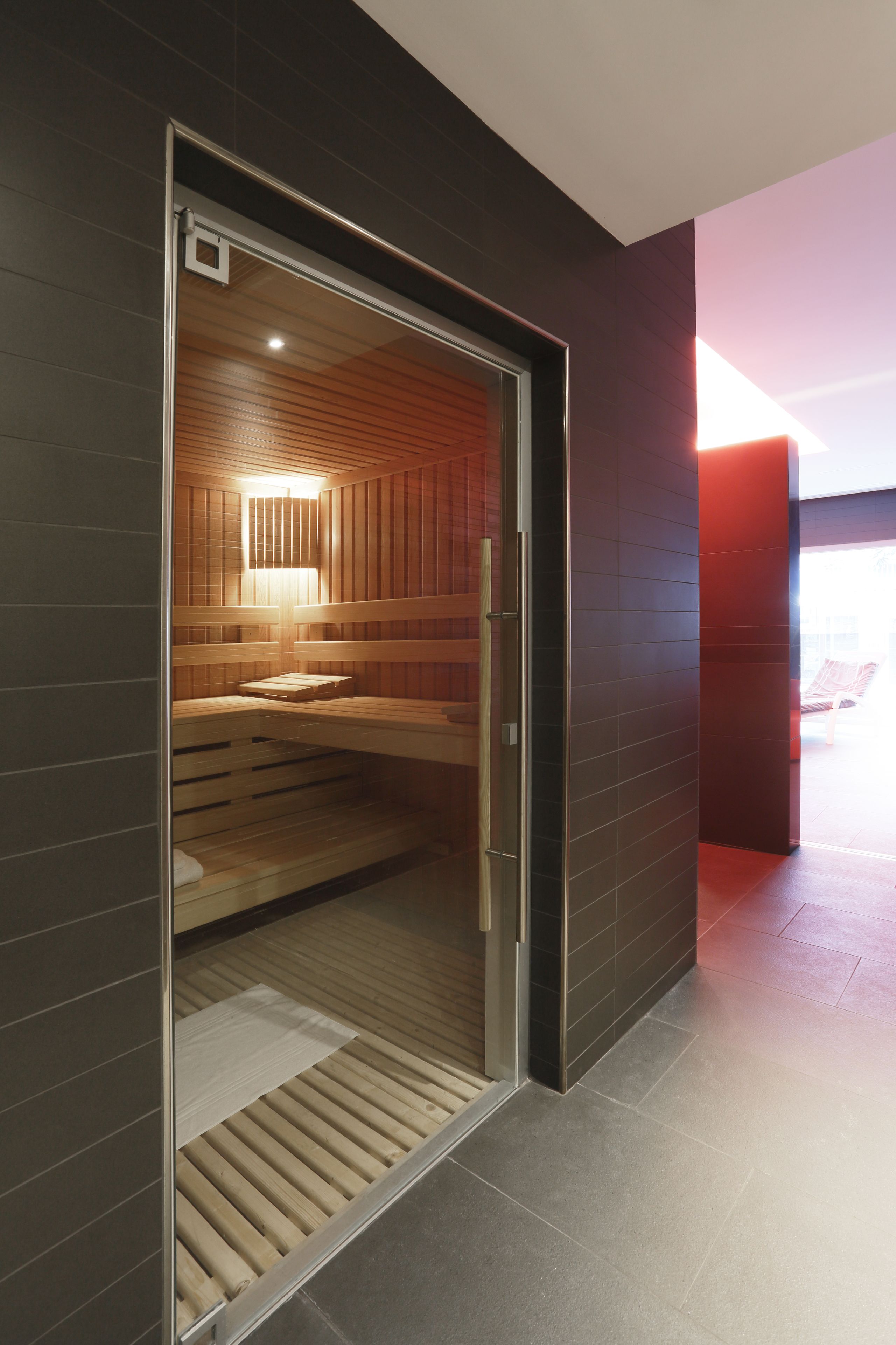 A modern sauna with a wooden interior, a glass door, and a bench.