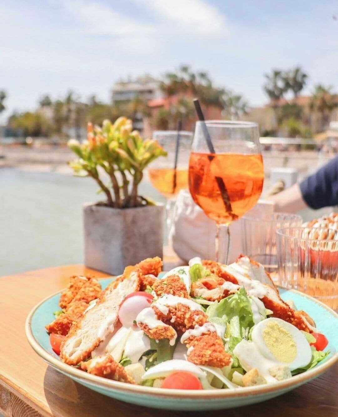 A plate of food with a salad, a boiled egg, and breaded chicken, with a drink in the background.