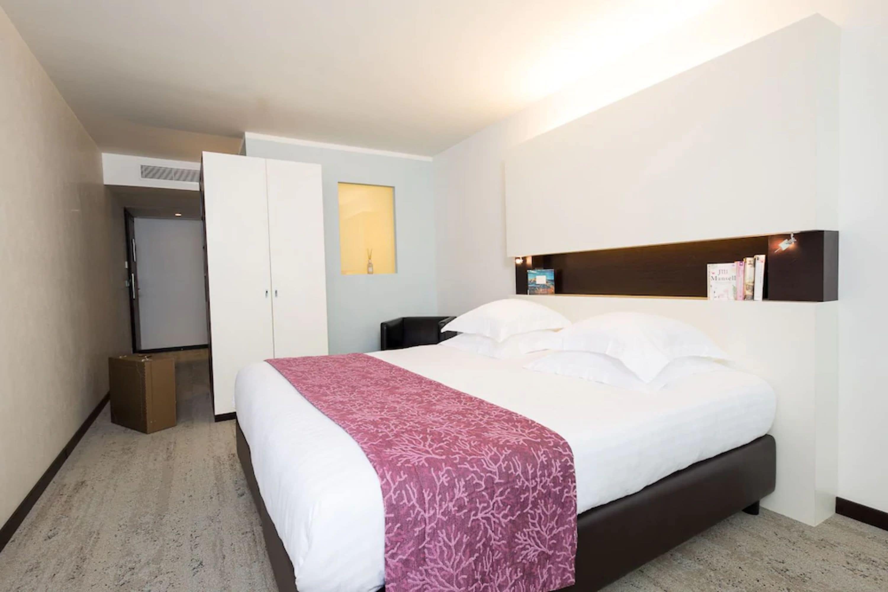 Een hotelkamer met een bed, een kledingkast, een nachtkastje en een plank met boeken.