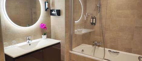 A modern bathroom with a glass-enclosed shower, a large mirror with a circular light, a white sink, and a bathtub.