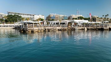 A waterfront hotel with outdoor seating areas, a stone pier, and buildings in the background.