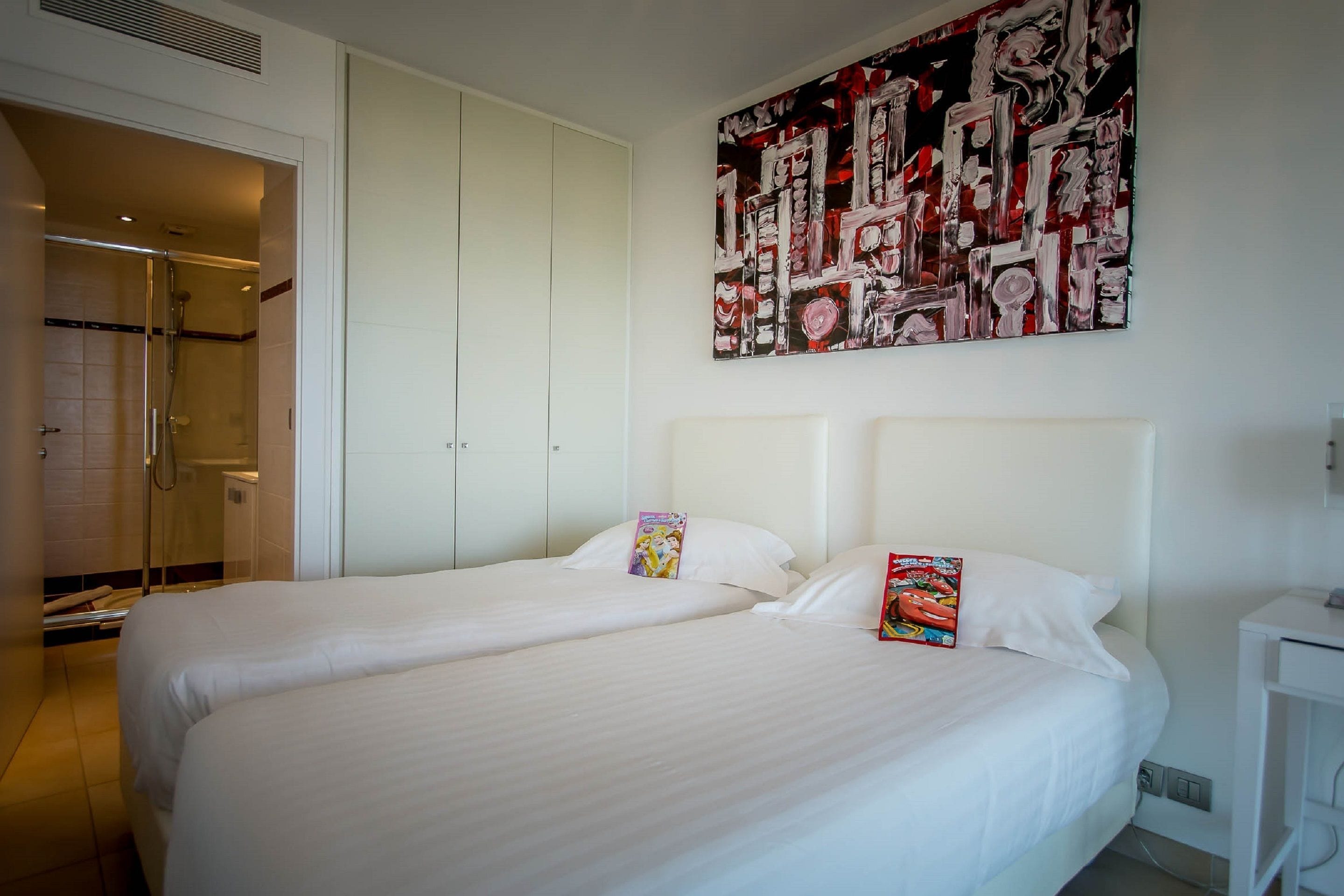 Ett hotellrum med två sängar, en stor, abstrakt målning på väggen och en rymlig klädkammare.