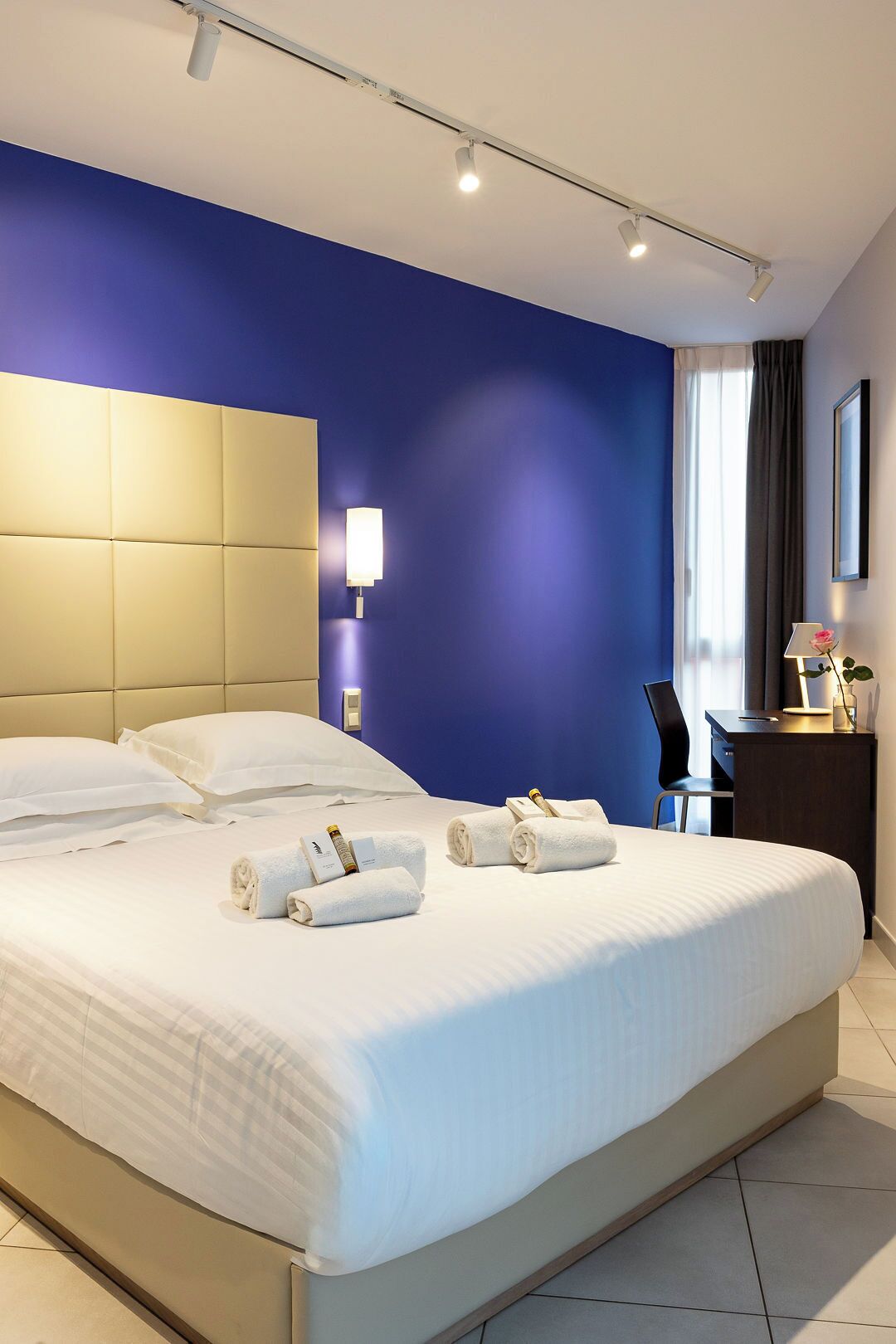 A modern hotel room with a large bed, a headboard, a desk, and a chair.