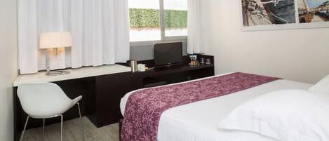 Una habitación de hotel con una cama, un escritorio con una silla, un televisor y una ventana con cortinas.