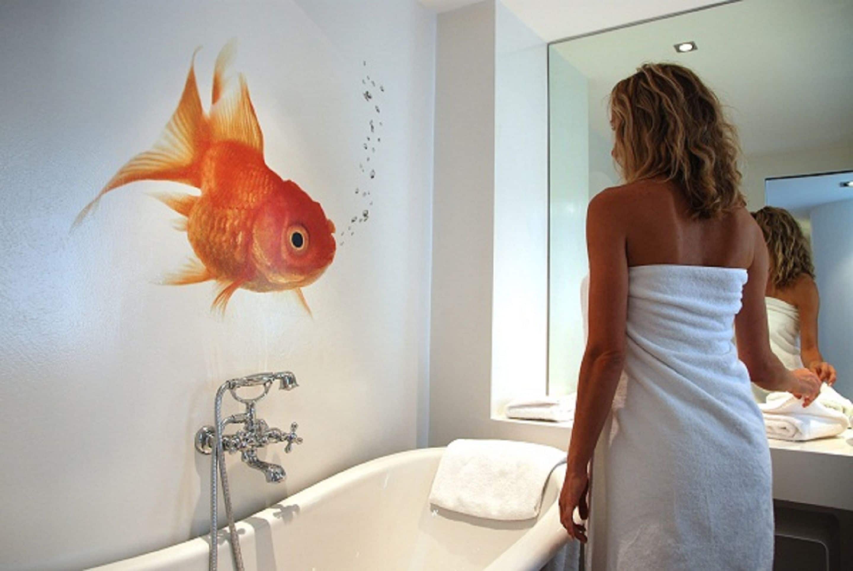 Un baño con un gran mural de peces, una bañera y un espejo que refleja a una persona.