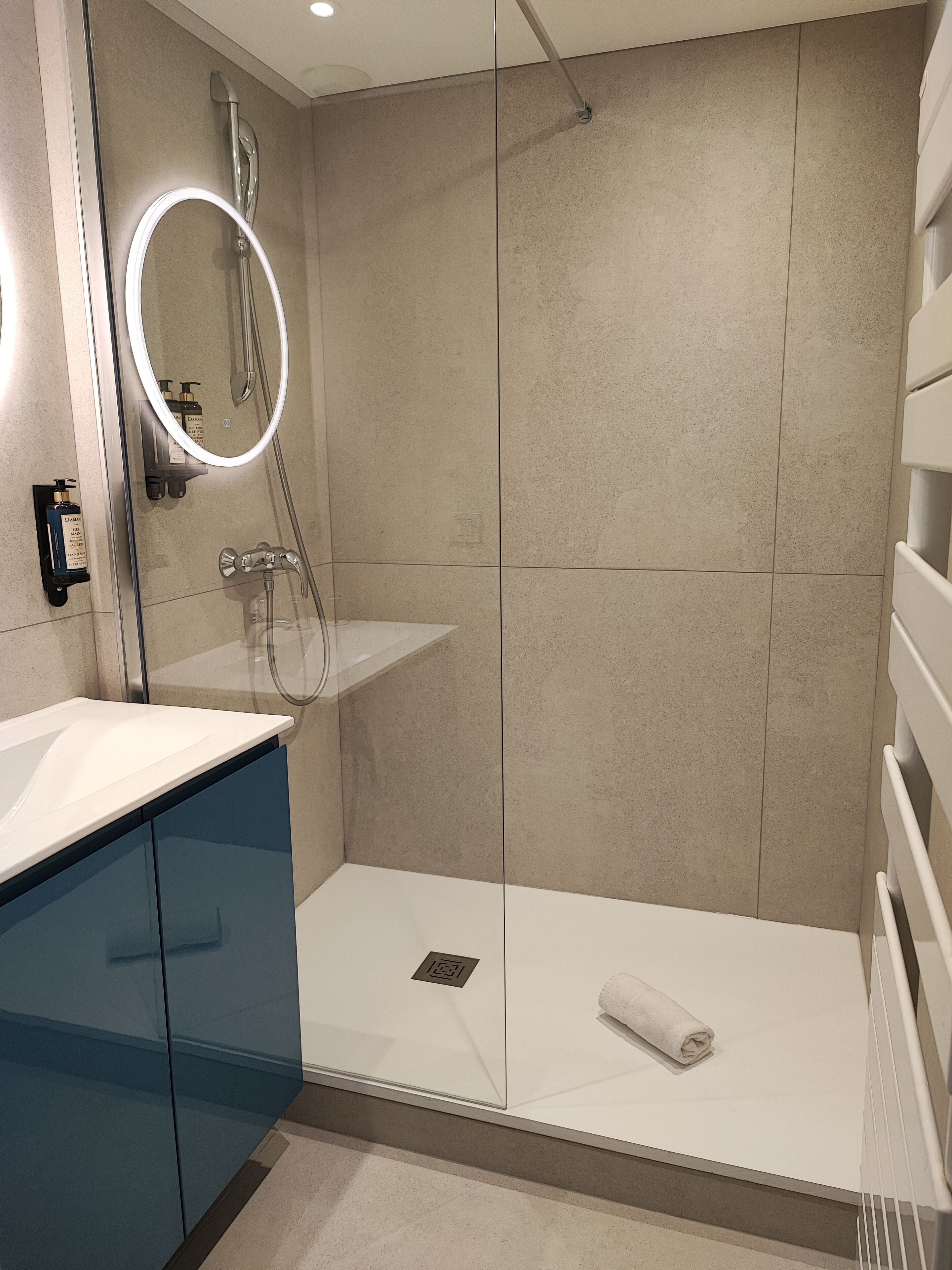 A modern bathroom with a glass-enclosed shower, a white sink, and a built-in mirror.