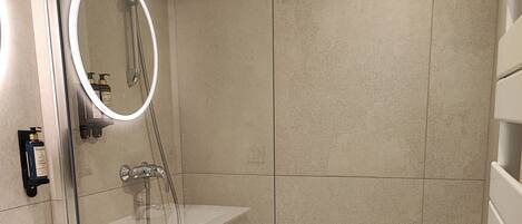 A modern bathroom with a glass-enclosed shower, a white sink, and a built-in mirror.
