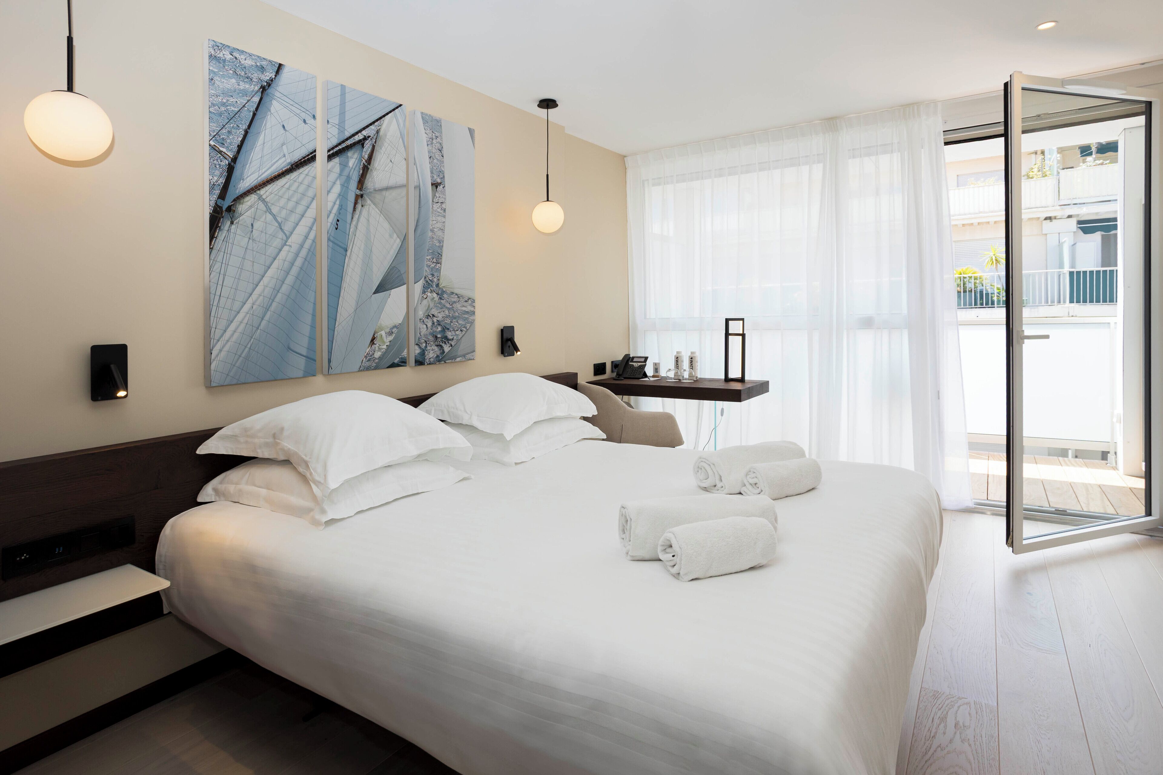 Ein modernes Hotelzimmer mit einem großen Bett, einem Nachttisch, einem Wandbild und Blick auf den Balkon.