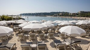 A beach with rows of white sun loungers and umbrellas, a clear sky, and a calm sea. - Royal Antibes (Antibes)