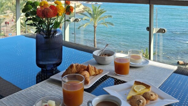A table with breakfast items, a vase of flowers, and a view of the sea. - Royal Antibes (Antibes)