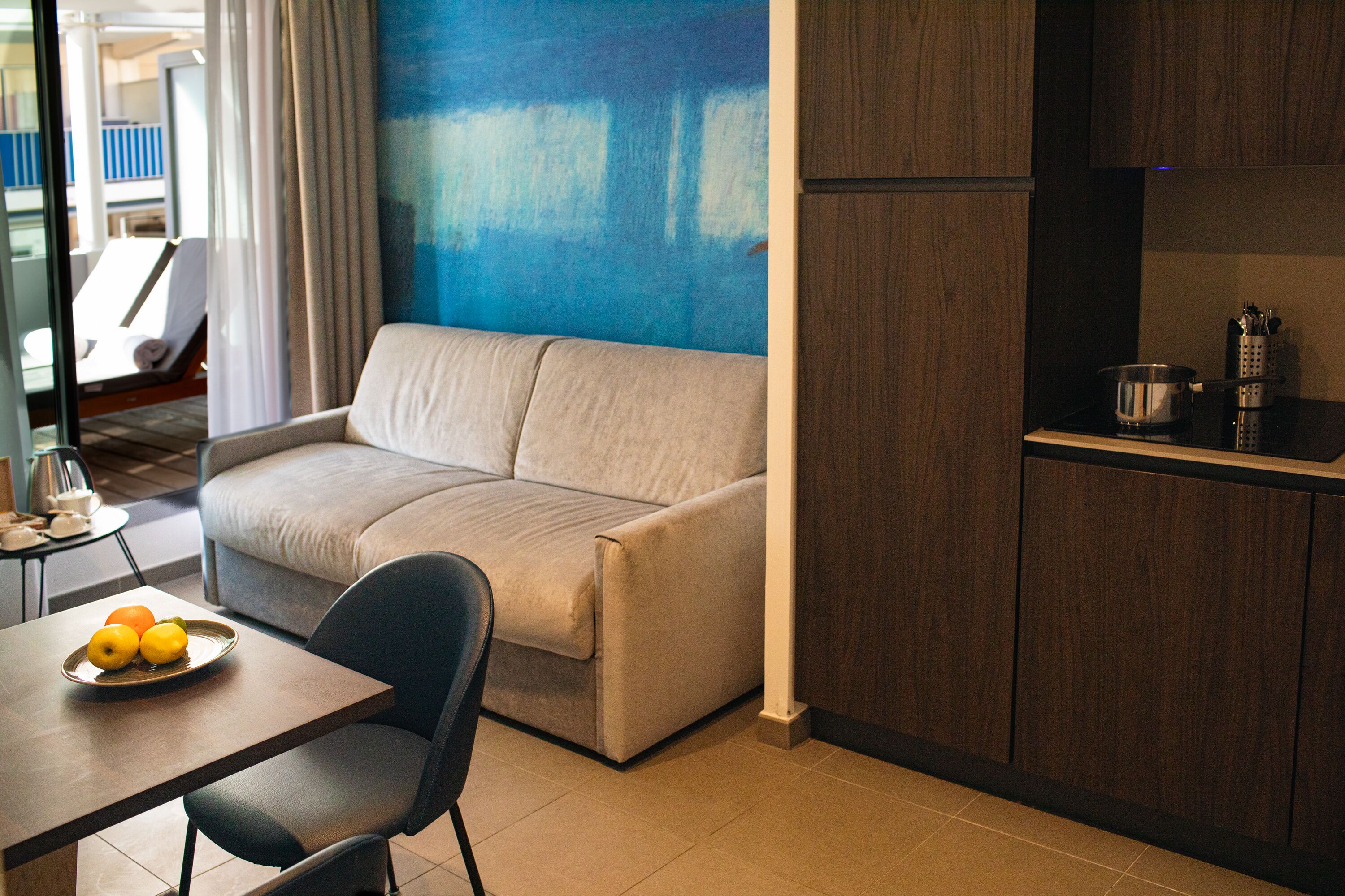 A modern living area with a sofa, a dining table with fruit, and a kitchen area with cabinets and a stove.
