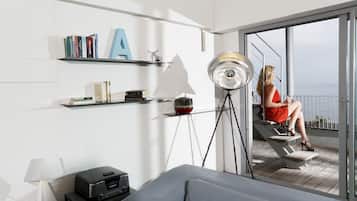 Una habitación moderna con sofá, lámpara, estantería y balcón con vistas al mar.