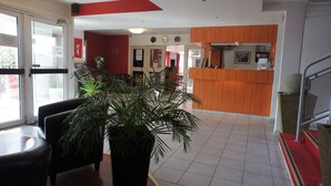 Un vestíbulo de hotel con una recepción, zona de estar y plantas en macetas.