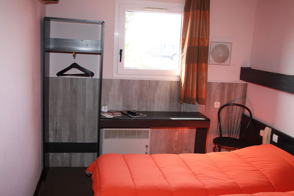 A compact room with a bed, a desk, a chair, a wardrobe, and a window with curtains.