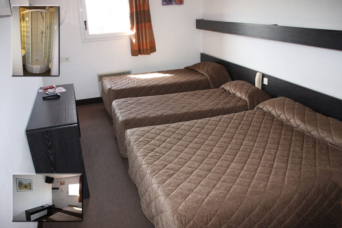 A hotel room with two beds, a desk, and a shower area.