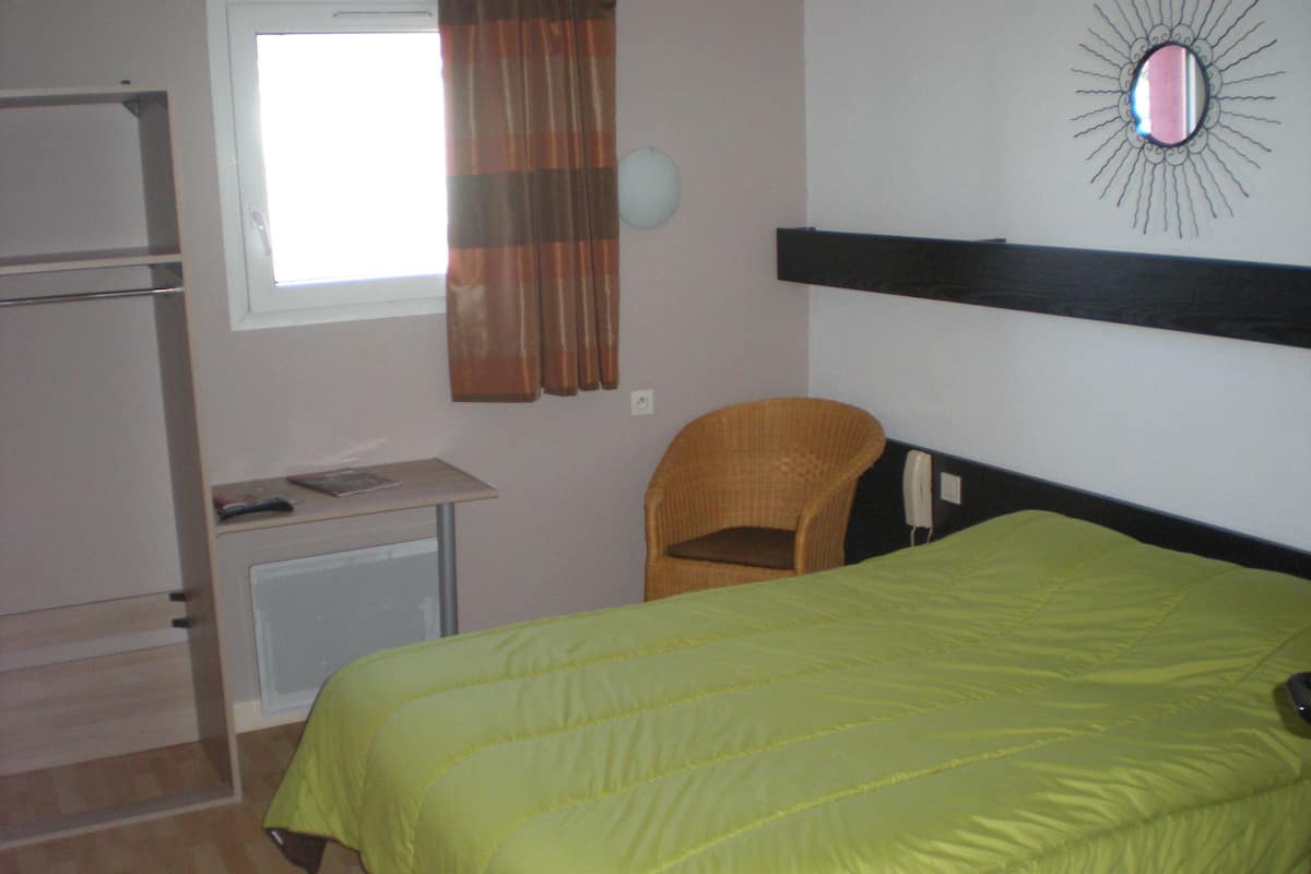 A room with a bed, a chair, a desk, and a window with curtains.
