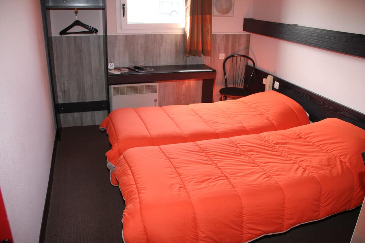 A small hotel room with two beds, a desk, a chair, and a window with curtains.