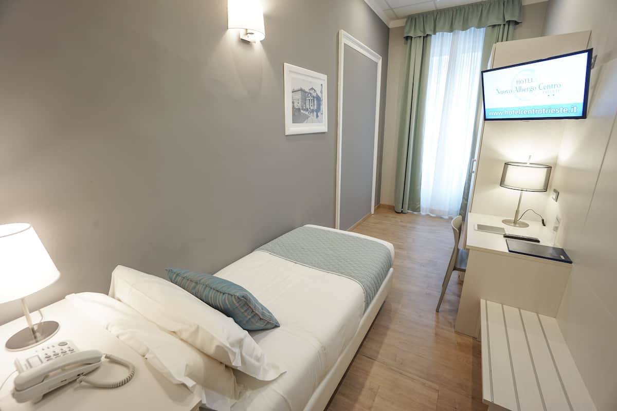 A hotel room with a bed, bedside lamp, phone, and a TV displaying the hotel name.