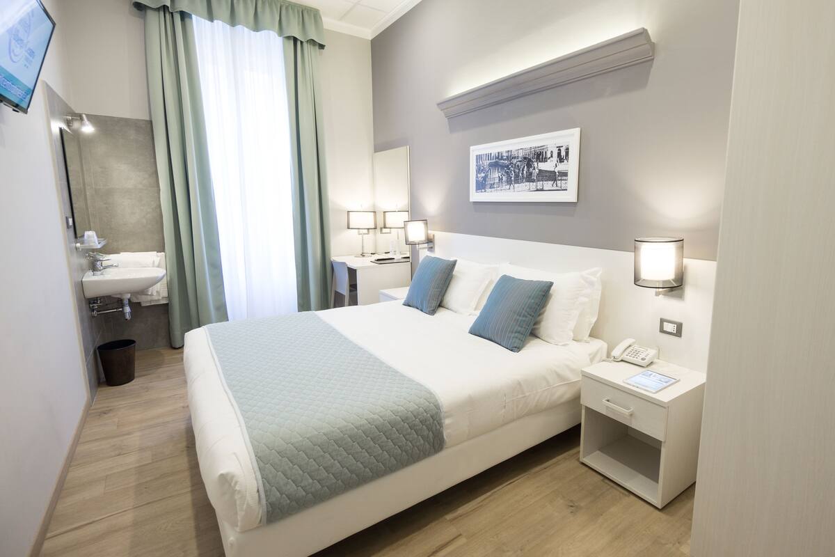 A hotel room with a bed, bedside tables, a desk, and a bathroom.