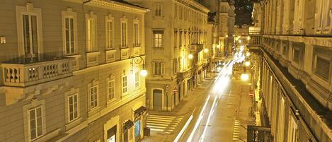 Vista nocturna de una calle con edificios históricos, un paso de cebra y farolas.