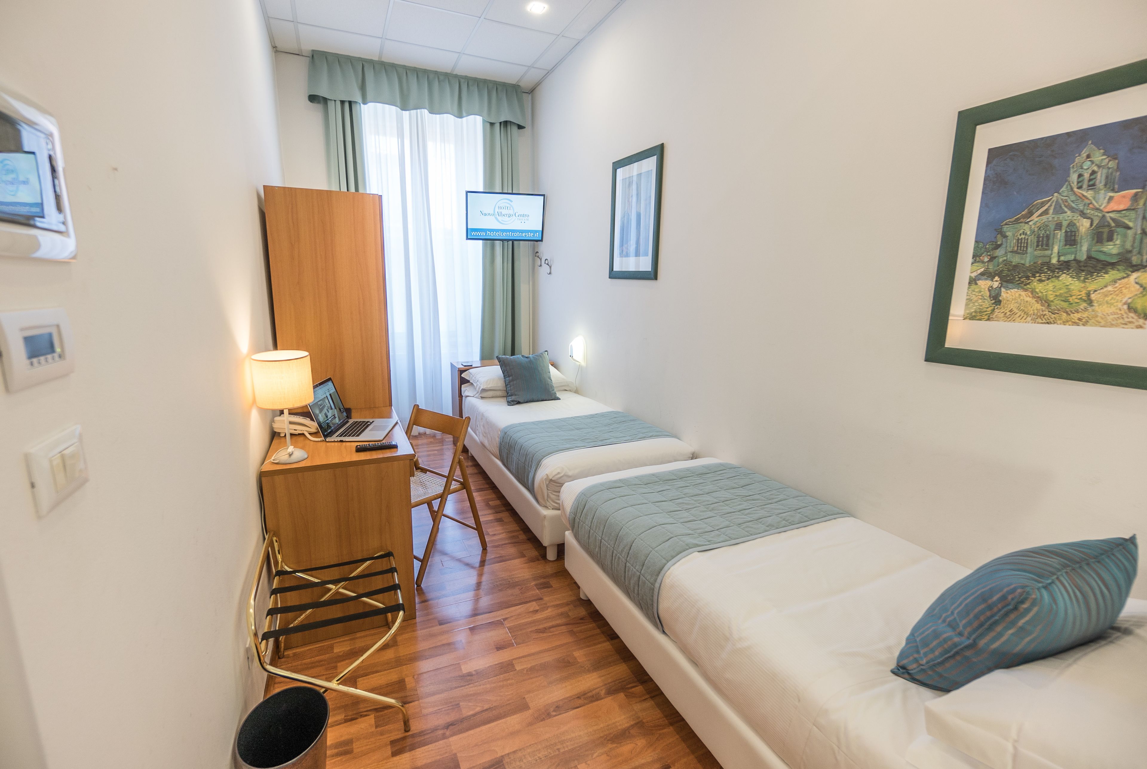 A hotel room with two beds, a desk with a lamp, a chair, a small table, and a framed picture on the wall.