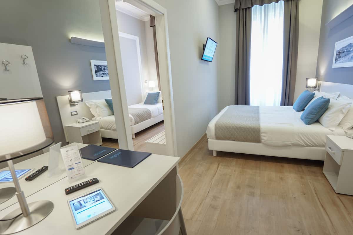 A hotel room with a bed, bedside tables, a desk with a computer, and a window with curtains.