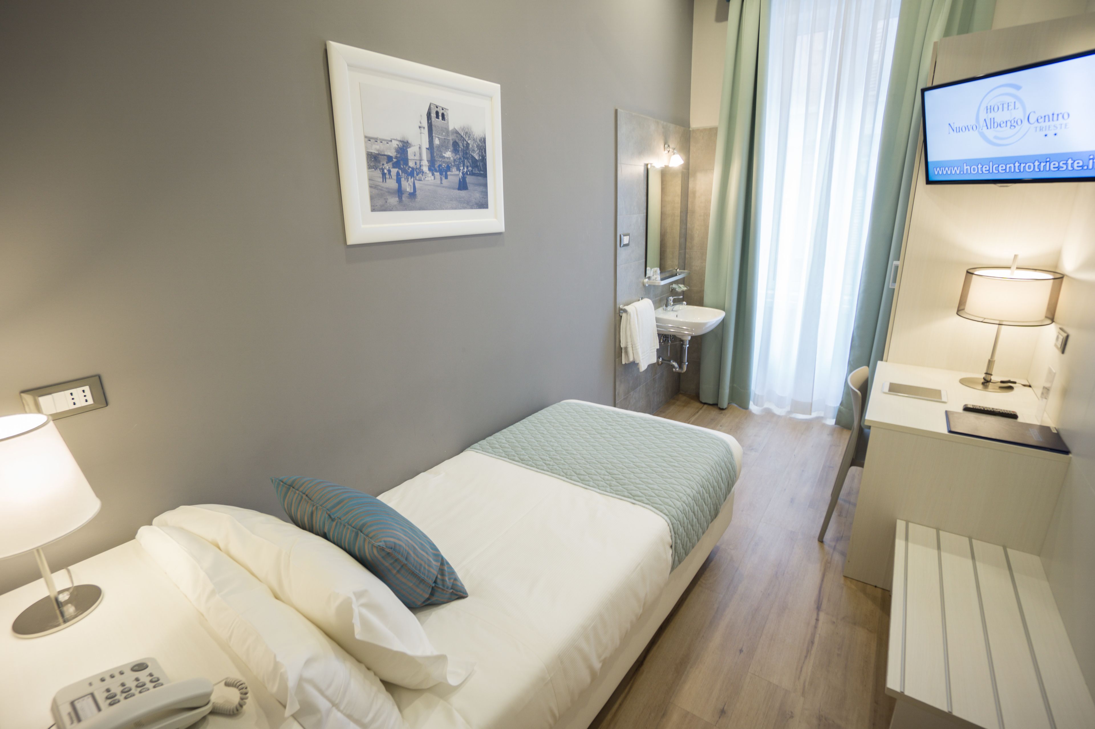 A hotel room with a bed, a bedside telephone, a mirror, a sink, and a television.