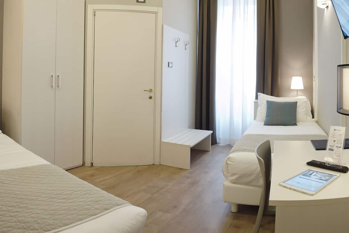 A hotel room with two beds, a desk with a chair, a television, and a bedside table with a lamp.