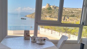 Una habitación con una mesa dispuesta para dos, vista al mar y una colina distante con edificios.